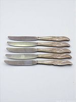 Five matching butter spreaders laid out showing both handles and blades