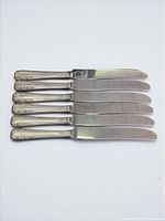 Six butter spreaders laid in a stack, showing handle detail and blades