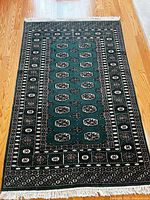 Full view of green patterned area rug with fringe