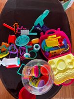 Wide view of Play-Doh tools, molds, compound cans jar, pink trays, various cutters on tabletop