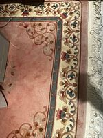 Corner of dusty rose rug with floral border and fringe