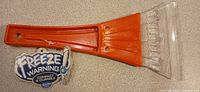 Single orange plastic ice scraper with tag and clear blade