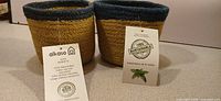 Two small natural jute baskets with green rims, Alkaso tags visible