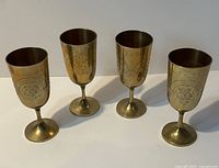 Four matching brass EPNS goblets standing upright showing decoration