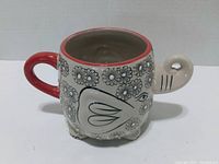 Front view of elephant-shaped mug showing floral design, red handle and trunk spout