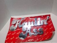 Front view of chrome metal "Haulin' Ass" decal on original red packaging