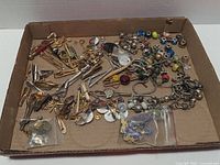 overview of entire lot showing tie clips, cufflinks, lapel pins, beads and bracelet in cardboard tray