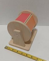 Side view showing wooden drum on base with red and orange panels and measuring tape for scale