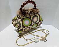 Front three-quarter view of purse lamp showing pattern, fur trim, handle, feet, cord, and switch