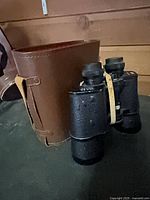 Black textured binoculars with brown leather carry case, elastic band around body