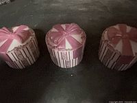 Three closed ceramic music boxes showing pink bows and striped sides