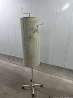 full view of beige cylindrical pegboard display on caster base