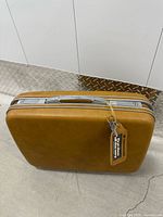Closed brown Samsonite hard-shell suitcase standing upright with hangtag attached