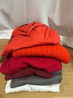 Stacked view of six folded tops showing colors and textures