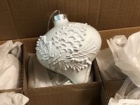 Open box showing compartmented packing and ornament with pinecone design