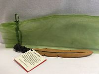 Full view of carved wooden eagle feather with green organza bag