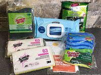 Group of sealed cleaning products: multiple packs of Scotch-Brite sponges, Pure antibacterial wipes, Clear Power wipes, dishwasher detergent sheets