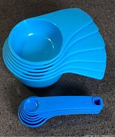 Stacked blue Tupperware measuring cups with attached handles alongside stacked measuring spoons