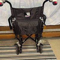 Rear view of folded Airgo transport chair showing logo, handles, wheels