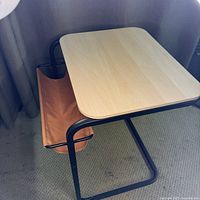 Angle view showing full C-shaped table, wood top, black frame, rust sling