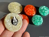 Close-up showing beige earring front and clip back, other colors blurred