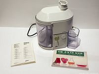 Juicer with pulp container, juice beaker, manual and book shown front view