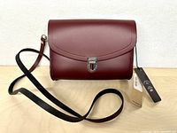Front view of oxblood leather pushlock satchel with strap and tags