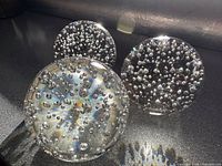 Three clear glass paperweights with bubbles displayed together on dark surface