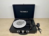 Turntable open showing platter, tonearm, controls and included power adapter