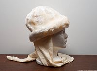 Side profile of cream faux fur hat with attached scarf flaps on mannequin head