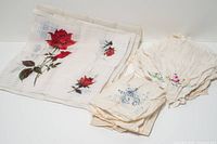 Group of embroidered handkerchiefs laid out, showing red rose piece and stack of others