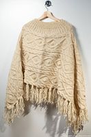 Front view of cream cable knit wool poncho with fringe