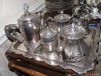 Full view of the silver tea and coffee service including pots, tray, and canister with detailed decorative motifs.