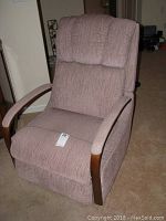 Front view of the mauve upholstered recliner chair with curved wooden armrests and a cushioned backrest.