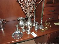 Full lot displayed on wooden surface including pewter vases, pitchers, candlesticks, candy dish, and brass coasters and plate stands.
