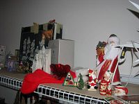 Shelving display of assorted Christmas decorations includes porcelain nativity figures in box, glass ornaments, Santa figurines, and other festive decor.