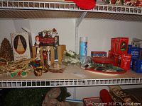 Shelf with various Christmas decorations including caroler figurines, Santas, linens, tins and candles.