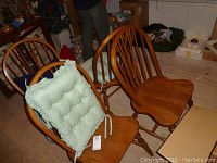 Set of four oak wooden chairs, two shown with green tufted cushions tied to backs, sitting on concrete floor amid cluttered background