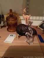 View showing amber glass turkey container with lid, pink-toned deer figurine, amethyst glass rabbit, clear glass deer, and small plastic deer on shelf.