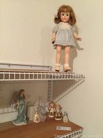 Full view of Effanbee doll on stand with blue dress and bow in hair standing on shelf.