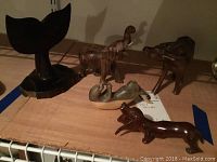 Photo showing all five carved wood animals: a whale tail carving on a stand, a yak, two two-tone otter figurines, and a glossy dachshund figurine