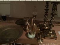 Heavy brass Yin Yang plate, multiple brass candle holders, and other decorative items on a wooden shelf