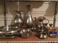 Overall view of multiple Royal Holland Pewter items arranged on a shelf including pitchers, vases, bowls, trays, and collectible stopper