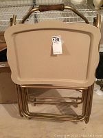 Stack of four gold-tone metal snack trays on top of matching rolling stand with wooden handle