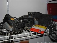 Three Black And Decker power tools on a white wire shelf: belt sander, planer, and finishing sander with cords and sandpaper