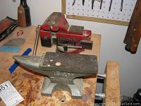 Full view of the red Fuller bench vice and gray metal anvil on a wooden workbench with some tools in the background