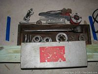 Top-down view of Fix N Save metal case with multiple threading dies inside and additional pipe tools including pipe wrench and threading die components.