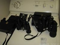 Full view of two binoculars with their cases and a manual, placed on top of a white appliance.