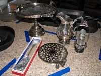 Pedestal silver plate serving tray with cut and etched designs surrounded by other items including pitcher, glass decanter in holder, thimbles, cake server and trivet.