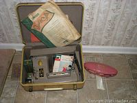 Singer model 301A sewing machine inside open suitcase case with owners manuals and sewing lesson material visible, pink plastic buttonholer case and white storage box of bobbins next to suitcase.